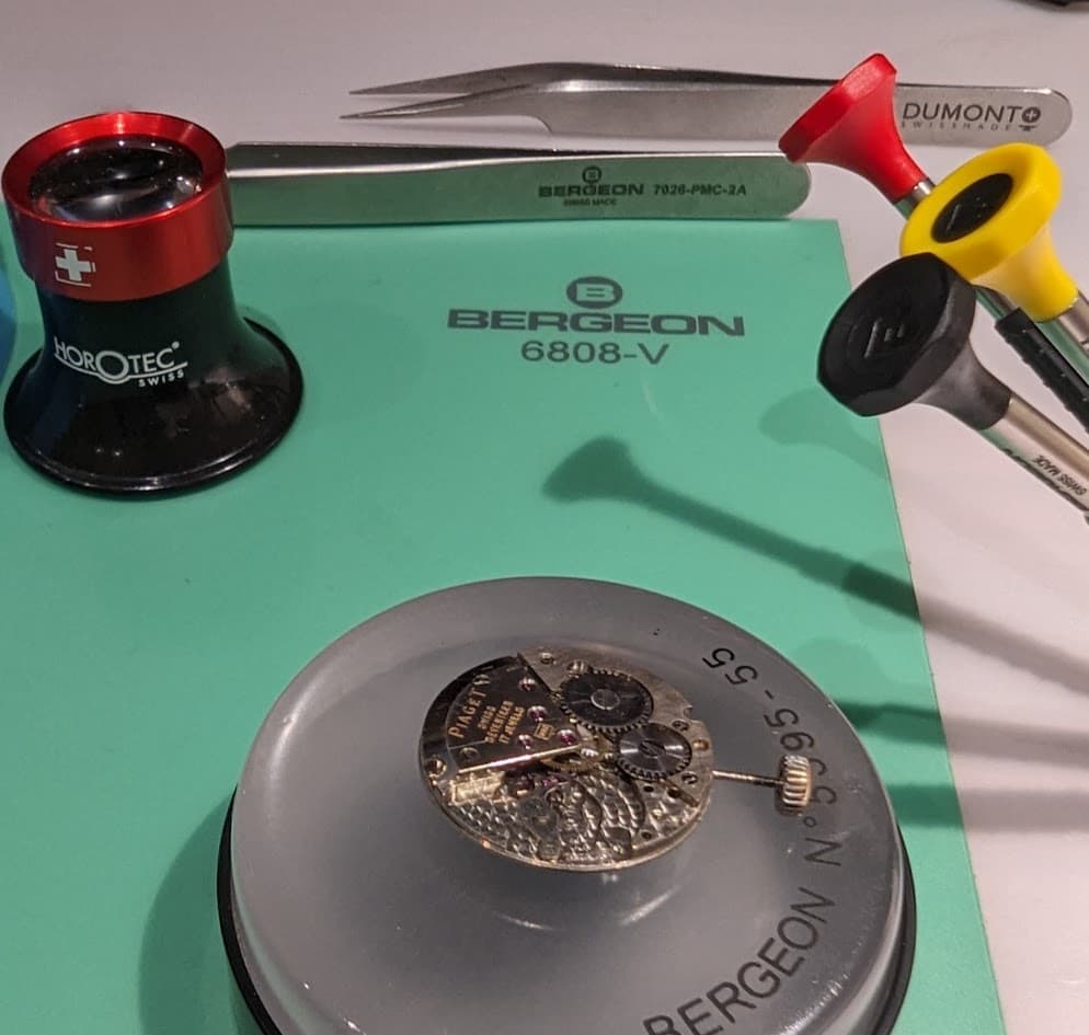 Watch repair tools and parts on a green mat